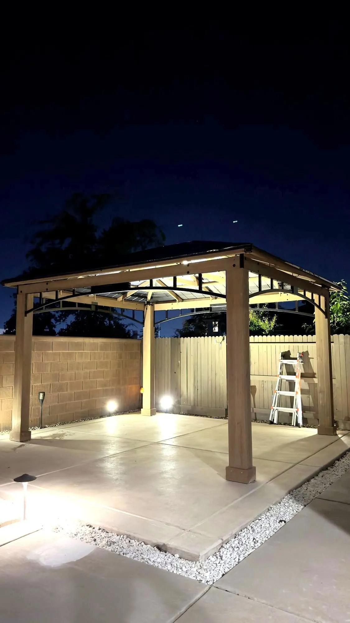 Backyard gazebo lit from below at dusk over a concrete pad