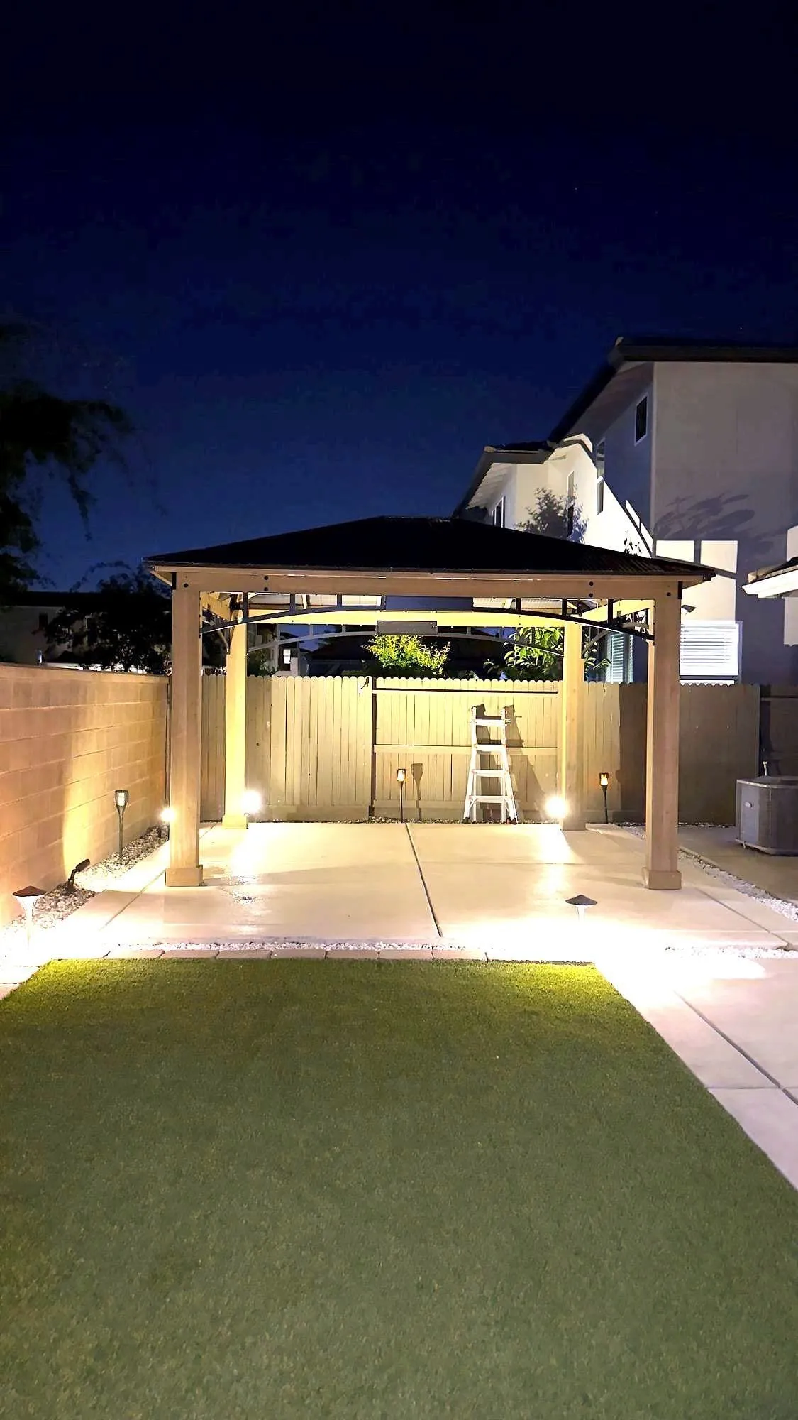 Backyard gazebo lit from below by ground uplights at night over a concrete pad