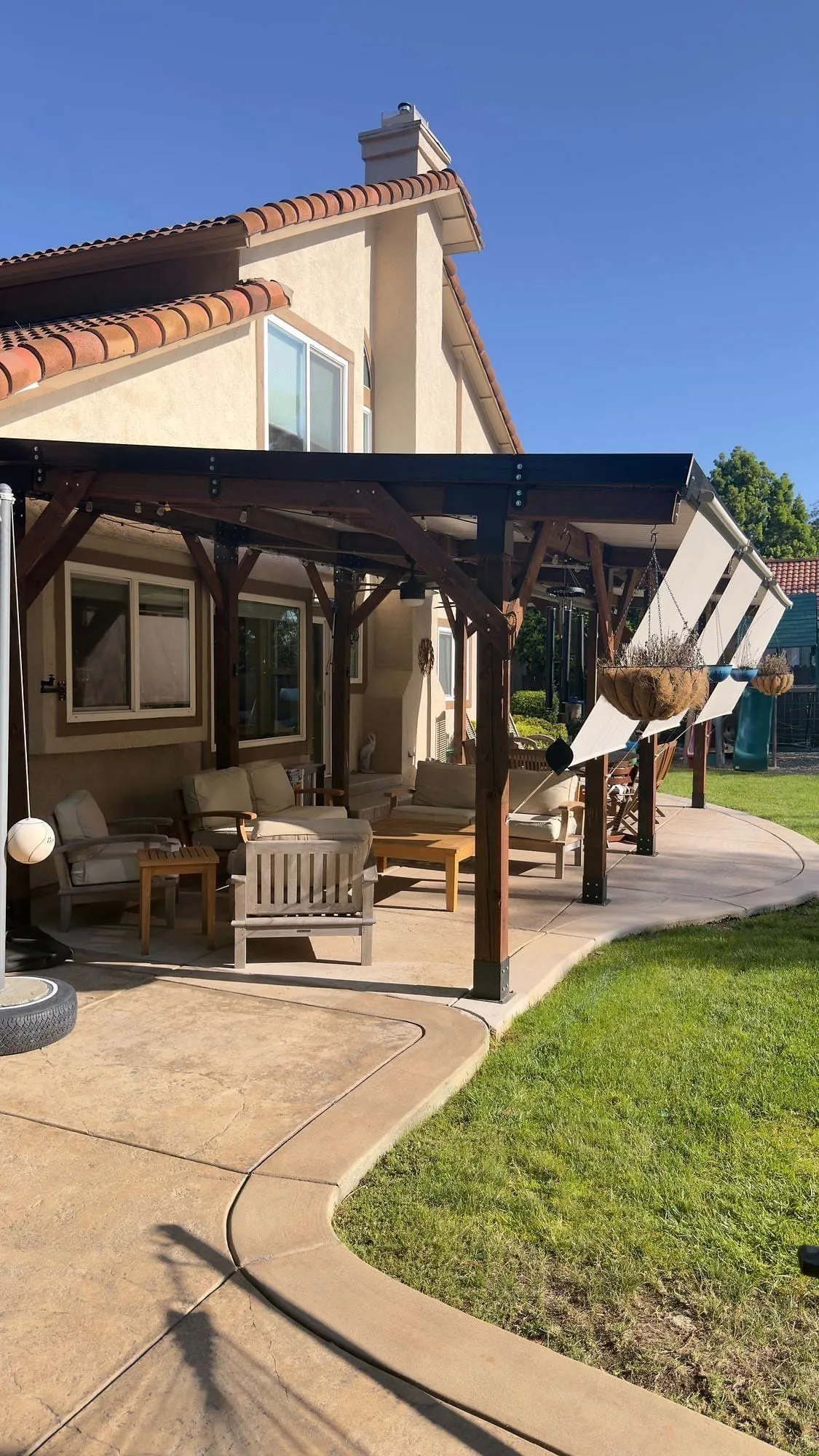 Timber covered patio with retractable shades over garden furniture at the back of a house