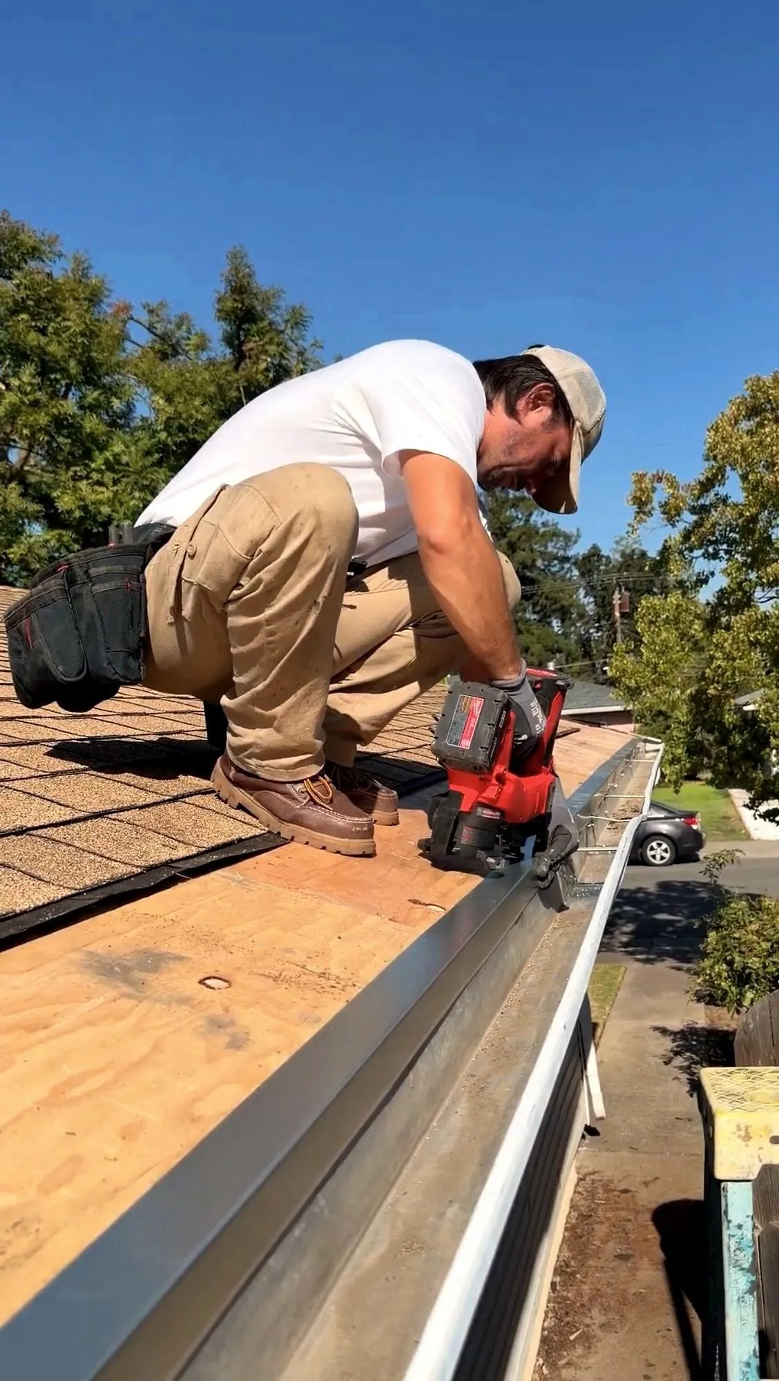 Serj kneeling on a roof cutting damaged timber out of the fascia line with a circular saw