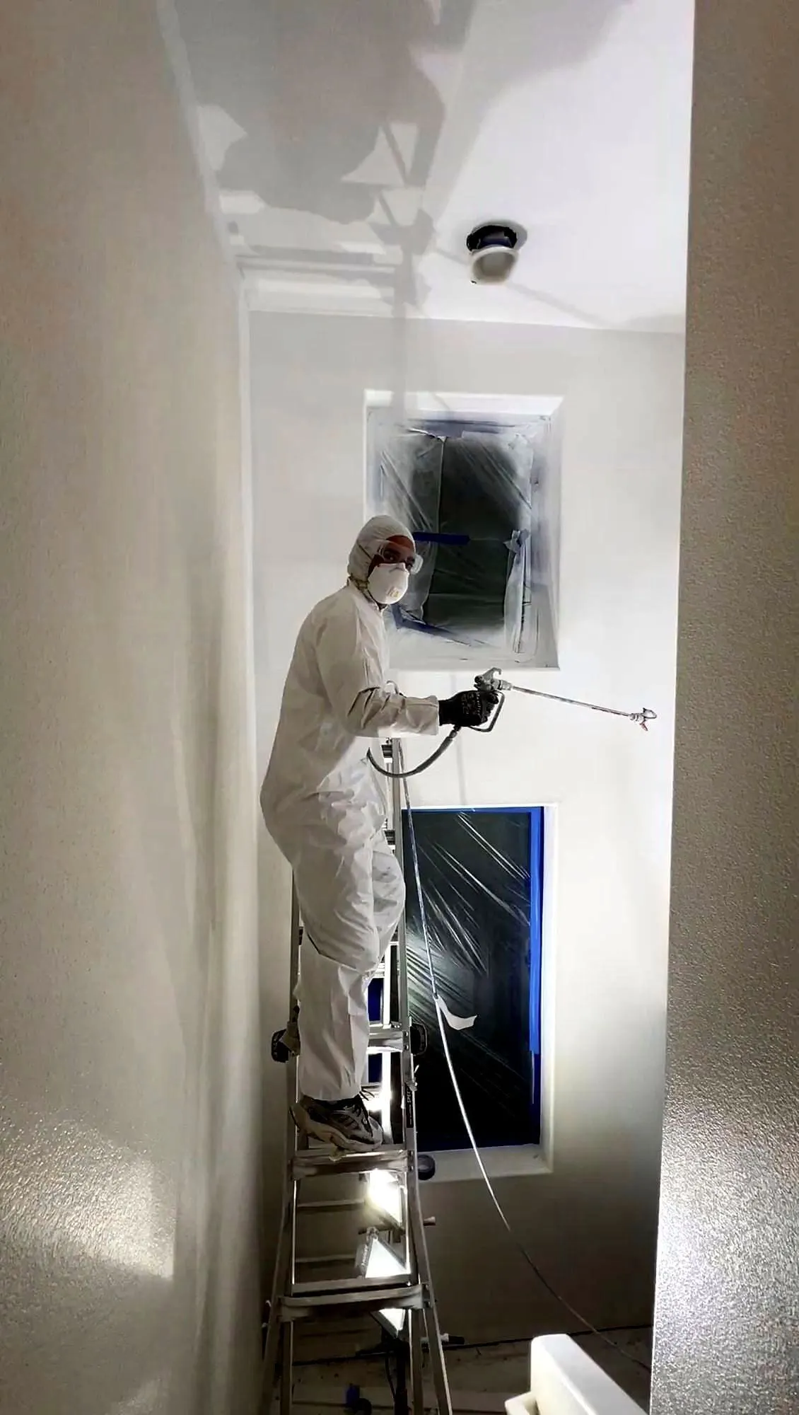 Spraying an interior wall in a full protective suit and respirator from a step ladder